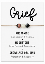 Crystals for grief A beaded therapy necklace on a card. The necklace features three gemstone beads: a pinkish-brown rhodonite, a white moonstone, and a black-and-white snowflake obsidian, strung on a thin tan cord.