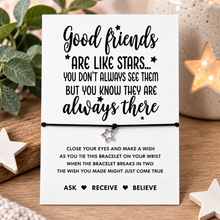 A black cord wish string bracelet with a small silver star charm displayed on a white message card that reads, 'Good friends ARE LIKE STARS.