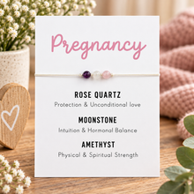 A delicate beaded pregnancy affirmation bracelet displayed on a white card. The card features pink 'Pregnancy' text at the top and black text listing the meanings of the beads: 'ROSE QUARTZ Protection & Unconditional Love', 'MOONSTONE Intuition & Hormonal Balance', and 'AMETHYST Physical & Spiritual Strength'.