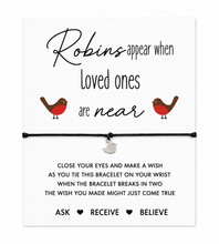 Sympathy, remembrance, memorial gift. A white card with printed sentimental text about robins and loved ones, featuring two small robin illustrations and a black bracelet laid across the centre. A tiny silver bird charm hangs from the bracelet.