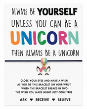 Unicorn gift. A square card for a unicorn-themed bracelet, with the phrase “ALWAYS BE YOURSELF UNLESS YOU CAN BE A UNICORN THEN ALWAYS BE A UNICORN” in black and colourful lettering. Unicorn rainbow charm on a black cord bracelet. Wish instructions on card.