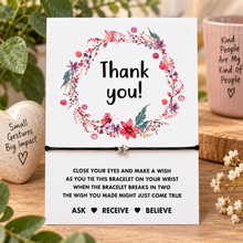 Thank you wish string bracelet. A white card with a floral wreath and the words 'Thank you!' above a black bracelet with a small silver star charm. The card includes a message about making a wish when the bracelet breaks in two.