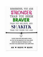 A motivational bracelet card featuring a black cord bracelet with a small silver star charm, displayed on a white card with colourful inspirational text. You are string wish bracelet. 