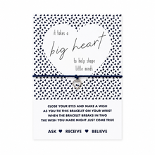 A heart-themed charm bracelet on a black blue cord, presented on its white and black patterned card packaging. The card features a large white heart with the words 'it takes a big heart to help shape little minds' and a silver heart charm. Teacher present 