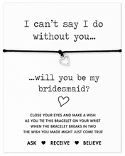 A white card with black printed text and a black cord bracelet with a small silver heart charm, designed as a bridesmaid proposal gift with the message 'I can't say I do without you. Will you be my bridesmaid wish bracelet.