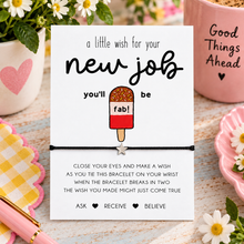 New job wish string bracelet. A square white card with a black bracelet attached, The card reads, 'a little wish for your new job you'll be' above a popsicle illustration with 'fab!' on it, and additional text below about tying the bracelet on the wrist when it breaks in two for a wish that may come true.