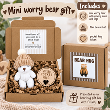 A 'Mini worry bear gift' presentation box set shown open with a small white plush bear wearing a beige knit hat, shredded brown paper filler, a round wooden token, and a branded card. A second closed box is shown beside it, along with an 'Includes' panel and gift message overlays on a soft neutral background.