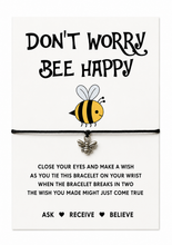 Don’t worry bee happy wish bracelet. A bracelet gift card featuring the phrase 'DON'T WORRY BEE HAPPY' in black lettering above a cartoon bee illustration. A black elastic bracelet with a small bee charm is displayed across the center.
