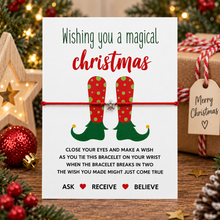 Christmas boots wish string bracelet. A Christmas-themed bracelet. The white card reads 'Wishing you a magical Christmas' with an illustration of red and green elf boots, tied with a red string bracelet with silver star charm.