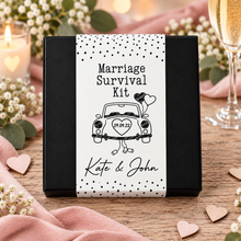 A black gift box with a white paper label reading 'Marriage Survival Kit' and personalised text 'Kate & John' with a car illustration. Unusual wedding gift. Customised wedding present 