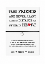 Friendship bracelet. A white card with black text and a small silver heart charm on a black cord, displayed against a white background. The card reads, 'TRUE FRIENDS ARE NEVER APART MAYBE IN DISTANCE BUT NEVER IN HEART' with a red heart symbol, and includes wish instructions below.