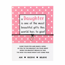 Birthday gift for daughter. A pink and white polka dot card with a message for a daughter, tied with a black string bracelet and a small silver heart charm, on a white background. Daughter wish bracelet 