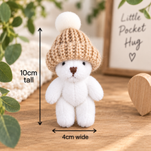 A small plush white bear wearing a beige knit hat with a white pom-pom, shown on a wooden surface with measurement arrows indicating 10cm tall and 4cm wide.