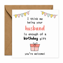 Birthday card for wife. A square white birthday card with a brown kraft envelope behind it. The card has a playful printed message that reads, 'I think me being your husband is enough of a birthday gift you're welcome!' with colorful bunting and a small gift box illustration.