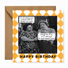 A square birthday card with a yellow and white diamond pattern border, featuring a black-and-white photo of two women with speech bubbles, and the text 'HAPPY BIRTHDAY' at the bottom. A brown envelope is placed behind the card on a white background.