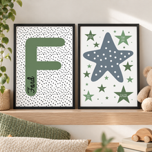 Boys room print set. Nursery wall art. Two framed personalised nursery art prints displayed side-by-side on a wooden shelf in a styled nursery setting. The left print features a large green letter 'F' with the name 'Finn' written vertically in black script on a white background with black polka dots.