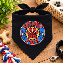 A black dog bandana with a tied top, featuring a colourful circular 'Spidey Pup' graphic on the front. Spidey pup dog bandana in black. Superhero dog bandana. Funny slogan dog scarf neck tie