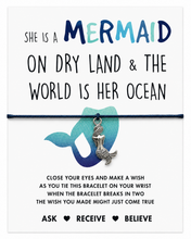 Mermaid-themed bracelet gift with the phrase 'She is a mermaid on dry land & the world is her ocean' and instructions below, featuring a black cord bracelet with a silver mermaid charm and a blue mermaid tail illustration on a white background.