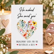 Wildflower Engagement seeds. A white greeting card with the text 'He asked She said yes' and 'Engagement seeds for the Butterflies & Bees!'  with a removable floral heart-shaped seed paper attached in the centre. Engagement gift.