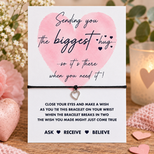 Sending you a hug wish string bracelet. A white card with a pink heart and black text says 'Sending you the biggest hug. Includes a silver heart bracelet 