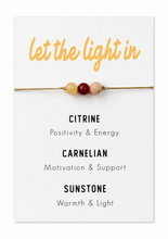 Natural crystal bracelet to let the light in. Healing crystals for seasonal affective disorder. A cord bracelet with three small beads displayed on a white card that reads 'let the light in' and lists the gemstone names Citrine, Carnelian, and Sunstone with their meanings.
