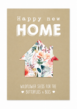 A square greeting card or print with a tan background and white text reading 'Happy new HOME' and 'WILDFLOWER SEEDS FOR THE BUTTERFLIES & BEES'. floral house-shaped removable seedpaper sits in the center, with watercolor-style flowers and leaves in pink, coral, green, and blue tones.