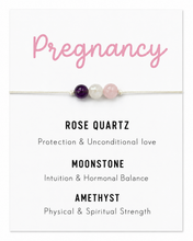 A white card displaying a pregnancy-themed beaded bracelet. The card features the word 'Pregnancy' in pink script at the top, a thin white cord with three beads (purple, white, and light pink) across the center, and three text sections below naming the stones and their meanings: Rose Quartz, Moonstone, and Amethyst.