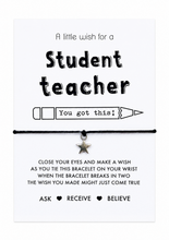 Student teacher wish string bracelet. A white rectangular card with black text and a pencil reading 'A little wish for a Student teacher You got this!' is displayed on a wooden desk. A black cord bracelet with a small silver star charm is tied across the centre of the card. Gift for a teacher in training. 