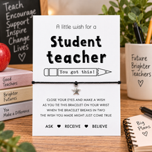 Student teacher wish string bracelet. A white rectangular card with black text and a pencil reading 'A little wish for a Student teacher You got this!' is displayed on a wooden desk. A black cord bracelet with a small silver star charm is tied across the centre of the card. Gift for a teacher in training. 