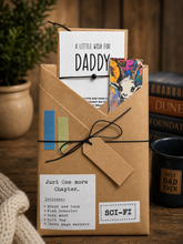 one more chapter book gift for daddy tied with black string, featuring a white card that reads 'A LITTLE WISH FOR DADDY' and a colorful illustrated bookmark or card peeking out. The box is labeled 'Just One More Chapter.