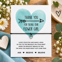 Flower girl wish string bracelet. A square white card with a watercolour heart and the words 'THANK YOU FOR BEING OUR FLOWER GIRL' above a black cord bracelet with a small silver heart charm.