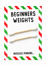 A novelty weight set labeled 'BEGINNERS WEIGHTS' with two cotton swab sticks as placeholder weights on a white card with red and green striped borders and the text 'MUSCLES PENDING.