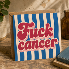 A square greeting card with bold retro text reading 'Fuck cancer' in pink letters over blue and cream vertical stripes, with a kraft brown envelope.