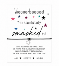 Gift of congratulations. A white rectangular card with printed motivational text and a black cord bracelet charm shown on the card. The card reads 'WoooooHooooooo! You absolutely smashed it!' with colourful star graphics and wish instructions below.