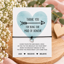 Maid of honour wish string bracelet. Silver heart on a black cord bracelet - A thank-you bracelet card. The card reads 'THANK YOU FOR BEING OUR MAID OF HONOUR' with a watercolour heart and arrow, and includes instructions for the bracelet below.