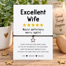 Wife wish string bracelet. A 'Excellent Wife' charm bracelet on a white card with humorous text, styled on a wooden table with a candle, potted plant, and wooden decor.