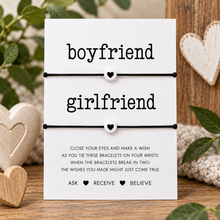 Boyfriend girlfriend wish string bracelets set. A white card with the words 'boyfriend' and 'girlfriend' above two black matching cord bracelets with small white heart charms. Gift for Valentine’s Day 