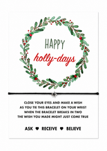 Happy holidays wish string bracelet. A festive white card with a green holly wreath and the words 'Happy holly-days' A black cord bracelet with a small silver star is tied across the centre of the card, with printed wish instructions below. Christmas gift 