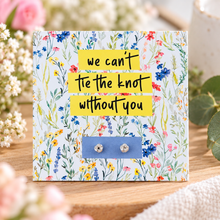 We can’t tie the knot without you earrings. Bridesmaid, flower girl, maid of honour proposal gifts. A square floral greeting card or gift card on a wooden surface, with yellow text reading 'we can't tie the knot without you' and two small silver stud earrings attached at the bottom.
