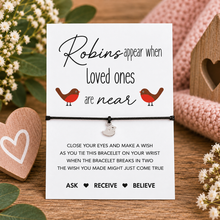 Robin wish string bracelet. A black cord bracelet with a small silver robin charm displayed on a white printed card. The card reads 'Robins appear when Loved ones are near' with two small robin illustrations, and includes instructions for using the bracelet.