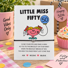 A wish string bracelet for a 50th birthday featuring a cartoon girl and the text 'LITTLE MISS FIFTY' and a bracelet with a star charm, styled on a tabletop with a pink cupcake, gift box, and decorative cards.