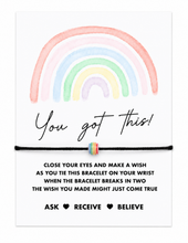 Encouragement gift. A white card with a pastel rainbow illustration at the top, the phrase 'You got this!' in black script, and a small striped charm on a black bracelet laid across the center. Below, printed text reads: 'Close your eyes and make a wish as you tie this bracelet on your wrist when the bracelet breaks in two the wish you made might just come true.