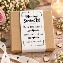 A square kraft paper gift box wrapped with a white paper label reading 'Marriage Survival Kit' and personalized text for Mr. & Mrs. A black gift box with a floral wedding-themed label reading 'Marriage Survival Kit' and personalised names 'Kate & John' with the date '29.09. Customised wedding gift. Unusual wedding present. Personalised marriage survival kit 