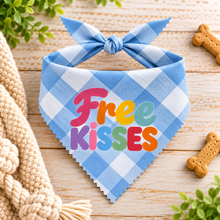 A blue and white gingham pet bandana with a bow, featuring the text 'Free KISSES' in colourful letters. Fun slogan dog bandana