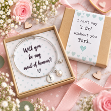 Maid of honour proposal bangle. Personalised silver bangle bracelet with a pearl charm and a round initial 'I' charm, presented in a kraft gift box with a printed message reading will you be my maid of honour? Maid of honour gift. Wedding favours 