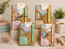 book gifts wrapped in floral paper and twine, each with a pen tucked inside, displayed on a tabletop with books, plants, and a cup in a styled home setting.