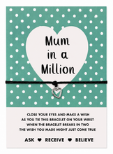 A 'Mum in a Million' charm bracelet presented on a white card with a teal and white polka dot background. The bracelet consists of a black cotton cord and a small silver heart charm.