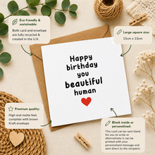 A white greeting card with the message 'Happy birthday you beautiful human' and a small red heart, shown with a brown kraft envelope on a beige fabric background. Decorative leaves, twine, dried flowers, and wooden clothespins surround it, with callout boxes describing eco-friendly sustainability, large square size (15cm x 15cm), premium quality, and blank interior personalization.