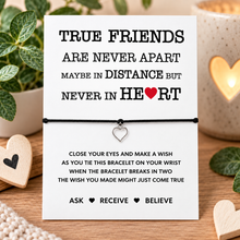 True friends wish string bracelet. A black cord bracelet with a small silver heart charm displayed on a white message card. The card reads, 'TRUE FRIENDS ARE NEVER APART MAYBE IN DISTANCE BUT NEVER IN HEART' and includes the words 'ASK RECEIVE BELIEVE' at the bottom.