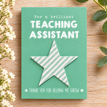 Teaching assistant wildflower seeds gift. A green greeting card with white text reading 'For a brilliant TEACHING ASSISTANT' and 'THANK YOU FOR HELPING ME GROW,' featuring a large striped plantable seeds star in the centre. Gift for teaching assistant. Thank you TA 